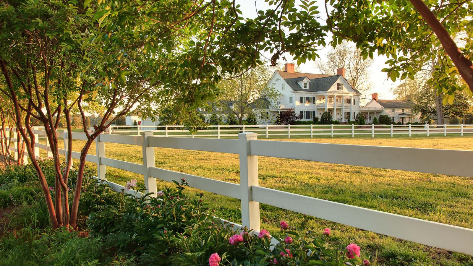 The Inn at Warner Hall at golden hour, framed by trees and a white fence